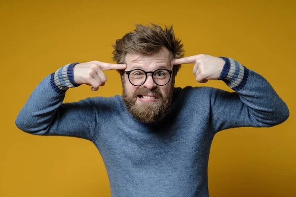 Angry shaggy man with glasses and an old sweater holds index fingers on his temples, proving to interlocutor that he is an idiot. — Stock Photo, Image