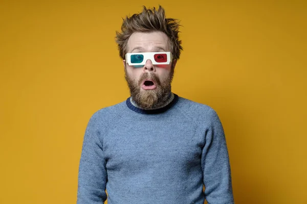 Shaggy, bearded man with 3D glasses and an old sweater, with a surprised expression on face and open mouth, on a yellow background. — Stock Photo, Image