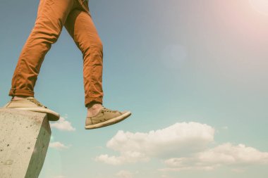 Beyaz kabarık bulutların üzerinde beton duvarla güvenli adımlar atan kişi mavi gökyüzünde, güneşli bahar gününde