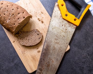 sert bayat ekmek ve bir parçası kesilmiş tahta kesme tahtasının üzerinde yatıyor, yanında paslı demir testeresi var.