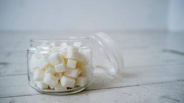 Beyaz renklerle boyanmış ahşap masada cam bir kavanozda beyaz şeker parçaları var.