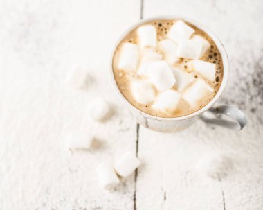 Bir fincanda sade kahve, eskinin üzerinde marşmelovlar, ahşap bir masa, üzerine pudra şekeri serpiştirilmiş.