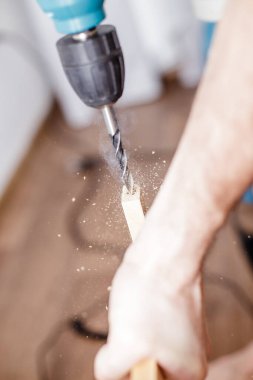 Evdeki odunlukta elektrikli matkap delen bir adam.