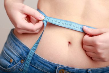 Açık tenli, mavi kotlu bir kadın ince bir bant kullanılarak ölçülür.