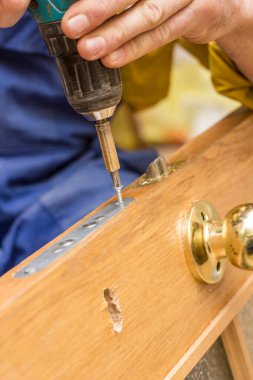 Marangoz tornavidayı kullanarak eski ahşap bir kapının kilidini takıyor..