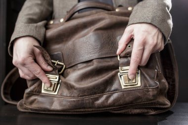 İzleyiciler arasında duran eski deri çantalı öğretmen, eski bir çantayı açar.