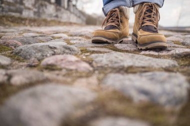 Botlu bacaklar, şehirdeki eski yosunlu kaldırım taşlarının üzerinde duruyor.