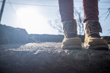 Gökyüzüne ve güneşe karşı beton bir yolda duran şık çizmeli bacaklar..