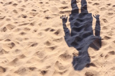 Güneşli bir yaz gününde sarı bir kumsalda duran bir adamın gölgesi.