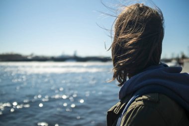 Güneşli bir günde, rüzgârda saçlarını uzatan esmer kız şehrin güneşli bir gününde, arka planda bulanık bir şekilde köprüyü ve gemiyi görebilirsiniz..