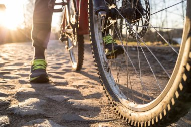 Bisiklet tekerleği, insan ayağının arka planındaki kaldırıma ve akşamları batan güneşe yakın.