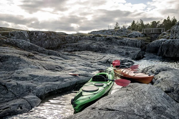 stock image Two kayaks are moored on the rocky shore, in the background you can see the old wooden bridge, cloudy sky and forest.