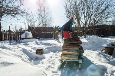 Zorluk çeken genç bir kadın, soğuk bir kış gününde, karla kaplı bir yolda yakacak odunuyla yaşlı bir tahta kızağı çeker..