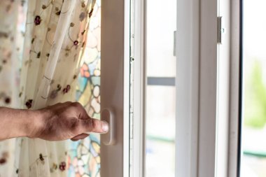 Bir erkek, güzel bir tülün arka planında bir sivrisinek ağıyla (PVC) penceresini açar. Yakın plan..