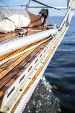 Adam bacak bacak üstüne attı ve yatın güvertesinde güneşli bir günde denizin ve gökyüzünün bulanık arka planında rahatça uzandı..