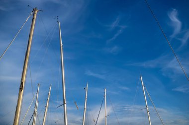 Mavi gökyüzüne ve bulutlara karşı güneş ışığında yatların direkleri, ılık yaz günü.
