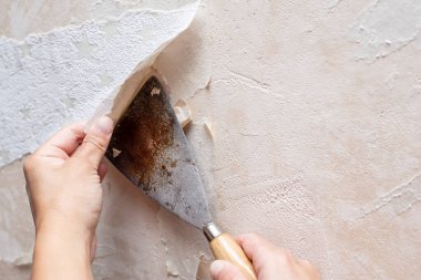 Odanın tamiri sırasında eski duvar kağıtlarını bir spatula yardımıyla kaldıran eller. Yakın plan..