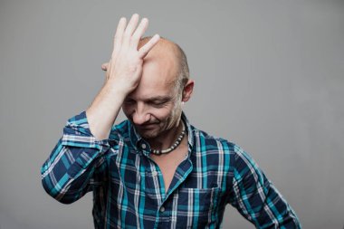 Mavi ekose gömlekli yakışıklı bir adam bir şey hatırlamaya çalışırken elini alnına koydu. Gri bir arka planda izole edilmiş. Yakın plan..