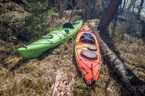 Two kayaks are in the spring forest near the camp, the sun and the smoke from the fire, near the lake.