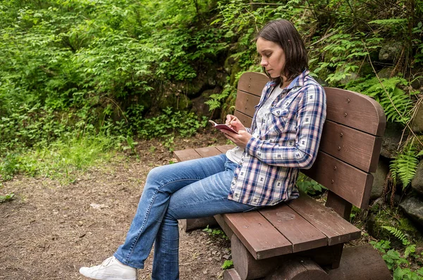 Söt Seriös Kvinna Sitter Träbänk Skogsparken Vid Stigen Och Antecknar — Stockfoto