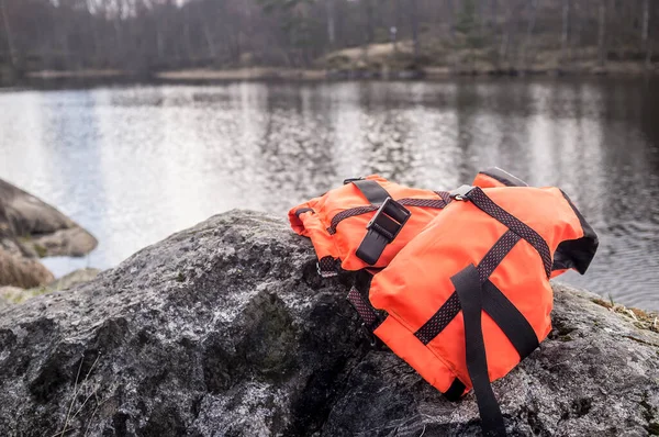 橙色的救生衣躺在湖畔的岩石上 背景是早春多云的一天 — 图库照片