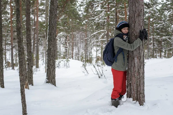 Cute woman hugging a tree in the winter forest. The concept of conservation of nature.