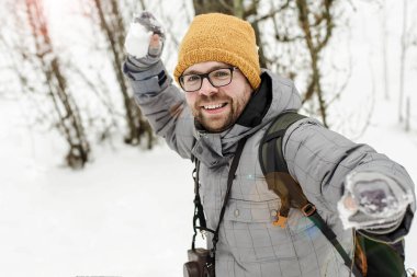 Kış eğlencesi Kameralı ve sırt çantalı neşeli, yakışıklı sakallı adam karların ve ormanın ortasında bir kartopu atmaya hazırlanıyor..