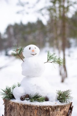 Küçük bir kardan adam bir kütüğün üzerinde, çam ormanının bulanık arka planında, dondurucu karlı kış. Yakın plan..