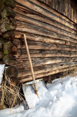 Paslanmaz, tahta saplı bir metal kürek, kırsal kesimde, soğuk ve güneşli bir günde, eski, çürük bir ağaç evin önünde duruyor..