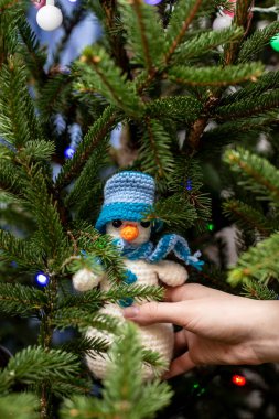 El, Noel ağacının dallarında çok renkli çelenklerle süslenmiş şapkalı ve atkılı şirin bir kardan adam tutuyor..