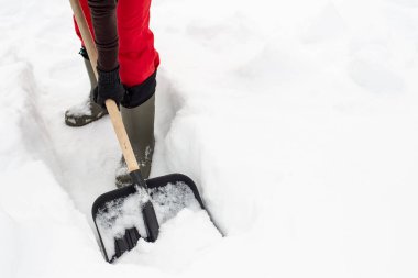 Tahta saplı siyah plastik kürek kullanan bir kadın karda yolu açar. Yakın plan..