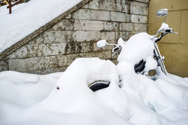 Rusya 'da kış. Evin duvarına yakın park edilmiş motosiklet neredeyse tamamen karla kaplı ve baharın başlamasını ve uzun yolculuklar için mevsimin başlamasını bekliyor..