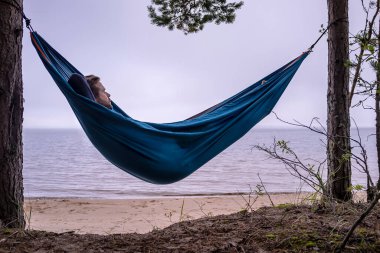 Turist, sakin bir çam ormanının yakınındaki gizli ıssız sahilde iz sürdükten sonra bir hamakta dinlenirken ciddi ve düşüncelidir.