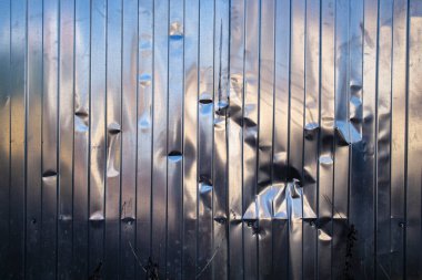 Mavi gökyüzünün ve binaların ayna yansımaları olan metal bir çitte x şeklinde bir göçük.