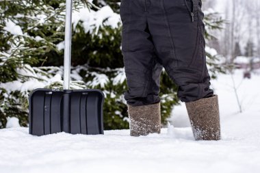 Keçeli ayakkabılı bir adam derin bir kar yığınında duruyor ve buz gibi bir kış günü kırsaldaki eve giden yolu temizleyecek..