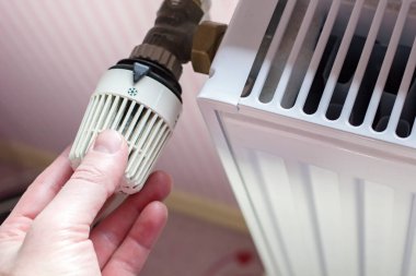Baharın gelmesiyle radyatör termostatını en aza indiren ve arka plandaki duvarda çizgili duvar kağıdıyla ısınan bir adamın eli. Yakın plan..