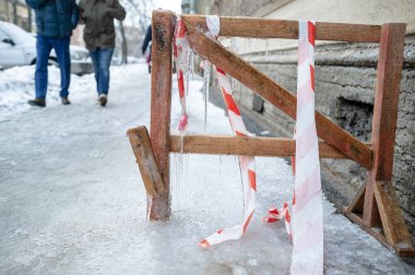 İnsanlar buz gibi sarsıcı kaldırımda yürüyor, kendi kendine yapılmış ahşap bir engelin donduğu, üzerinde buz sarkıtları asılı ve şehirde kış günü koruyucu bir bantla..