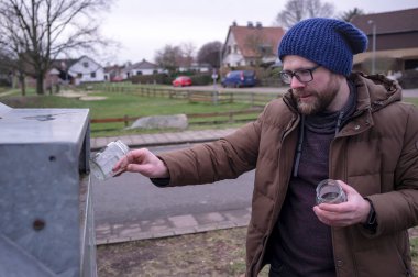 Kafkasyalı genç bir adam, Avrupa 'nın bir eyaletinde, konserve bebek mamasından kullanılmış beyaz cam kavanozları geri dönüşüm konteynerine atıyor..