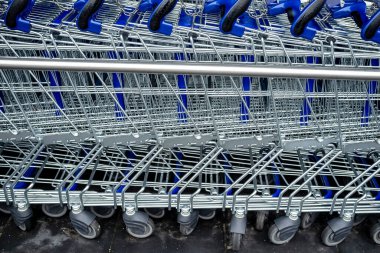Mağazanın yanında duran, tekerlekleri ve zincirleri olan mavi metal market arabalarının yan görüntüsü.