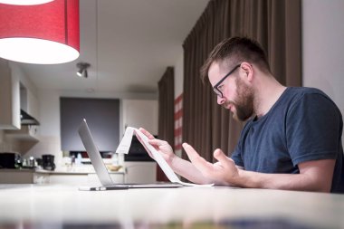 Mutfakta dizüstü bilgisayarın yanında oturan, mali işlerle ilgilenen Kafkasyalı genç adam şaşırmış ve mutsuzmuş.