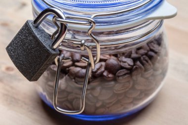 Closed metal lock on a transparent glass jar with a lid, in which coffee beans, against the background of a wooden table. Concept of a healthy lifestyle. Close-up. clipart