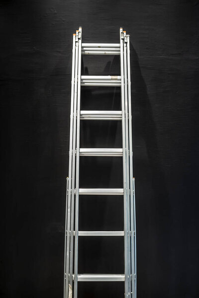 metal staircase stands near a beautifully textured black concrete wall lit from above
