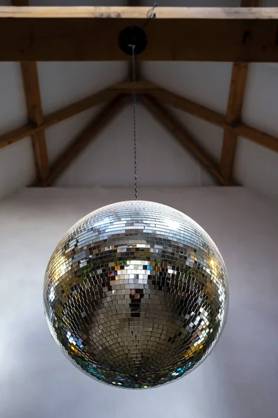 Mirror, brilliant, reflective disco ball hanging on a chain from the ceiling. Close-up.