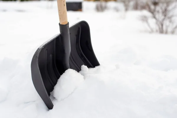 雪と茂みの背景に 雪のドリフトに立って木製のハンドルを持つ黒いプラスチック製のシャベル Vselskoyエリア ストック写真