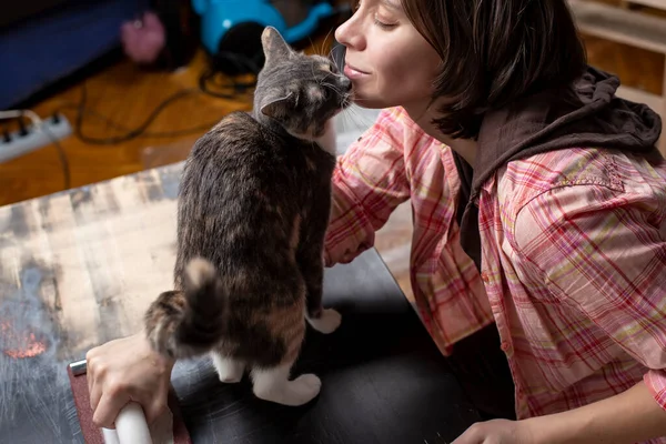 Woman prepares the surface for painting and sanding by hands an old wooden black table with a manual carpentry sandpapers holder, a beloved cat stands next to her and fondles her face. Home repairs. — Stock Image Woman Prepares Surface Painting Sanding Hands Old Wooden Black Table Royalty Free Stock Photos