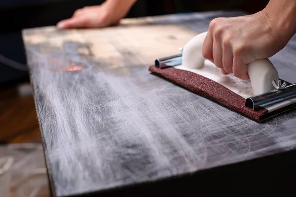 Person prepares the surface for painting and sanding by hands an old wooden black table with a manual carpentry sandpapers holder — Stock Image Person Prepares Surface Painting Sanding Hands Old Wooden Black Table Stock Picture