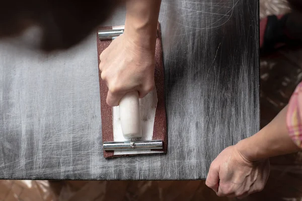 Top view on woman prepares the surface for painting and sanding by hands an old wooden black table with a manual carpentry sandpapers holder — Stock Image Top View Woman Prepares Surface Painting Sanding Hands Old Wooden Stock Picture