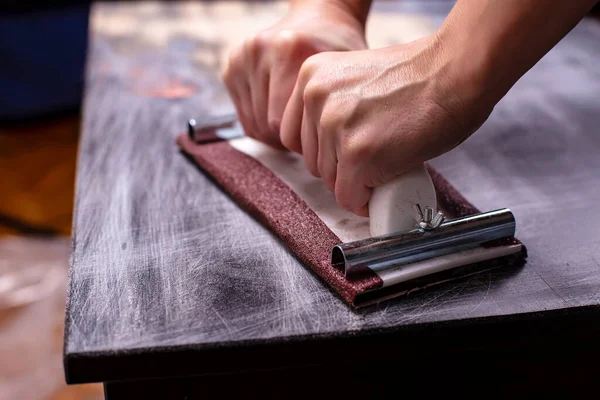 Person prepares the surface for painting and sanding by hands an old wooden black table with a manual carpentry sandpapers holder — Stock Image Person Prepares Surface Painting Sanding Hands Old Wooden Black Table Royalty Free Stock Photos