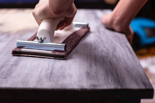 Person prepares the surface for painting and sanding by hands an old wooden black table with a manual carpentry sandpapers holder — Stock Image Person Prepares Surface Painting Sanding Hands Old Wooden Black Table Royalty Free Stock Images