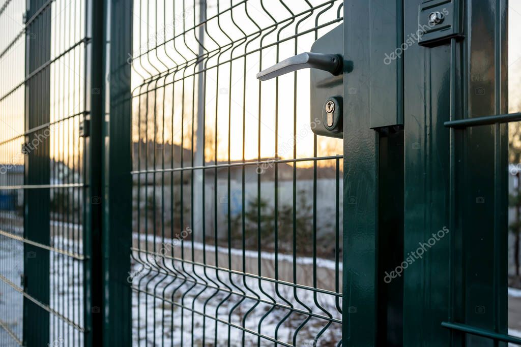 Entrance to the playground of fence and the wicket of the welded wire mesh green color with a metal lock and handle.
